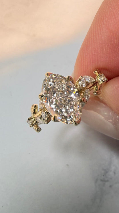 A close-up of a hand holding a gold ring with a large clear gemstone cluster, set against a light marble surface.