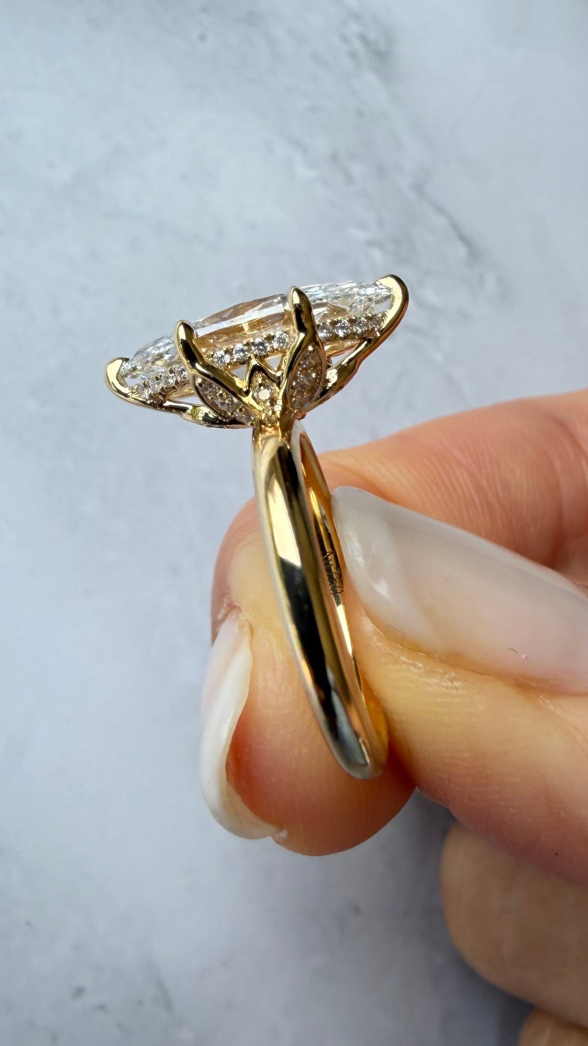 A close-up of a gold ring with a diamond cluster setting held by a hand against a light marble background.