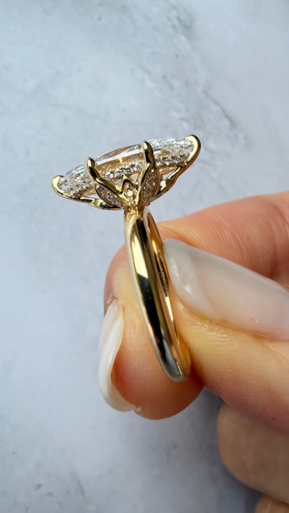 A close-up of a gold ring with a diamond cluster setting held by a hand against a light marble background.